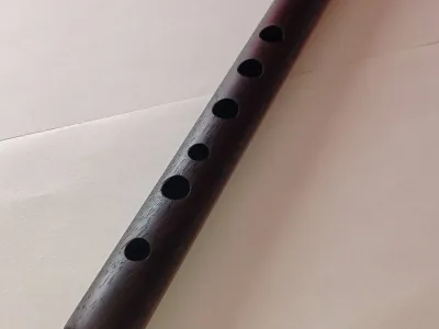 Quena de sándalo negro africano sobre una mesa. Se ven todos sus orificios frontales.